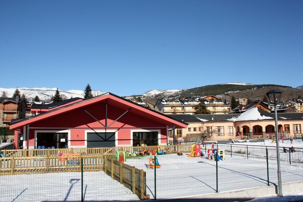 Pla obert on es veu part de l'edifici de la nova Escola Jaume I de Llívia (Cerdanya) i la Llar d'infants Els Esquirolets amb alguns alumnes jugant amb la neu al pati i l'antiga escola al fons. Imatge de l'11 de gener de 2021 (Horitzontal).